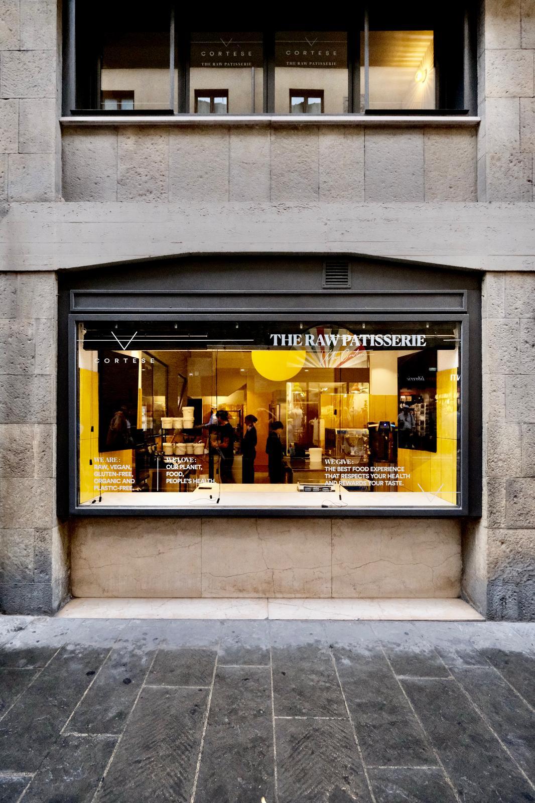 Vetrina esterna Cortese The Raw Patisserie Firenze · edificio storico in pietra · scritte vegan raw organic